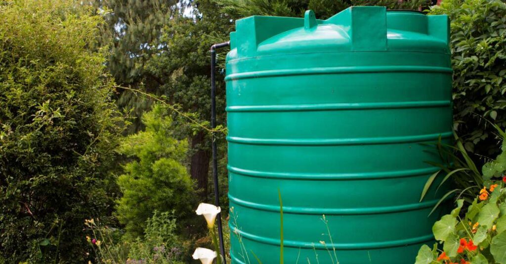Large green water tank in lush garden surrounded by plants and flowers